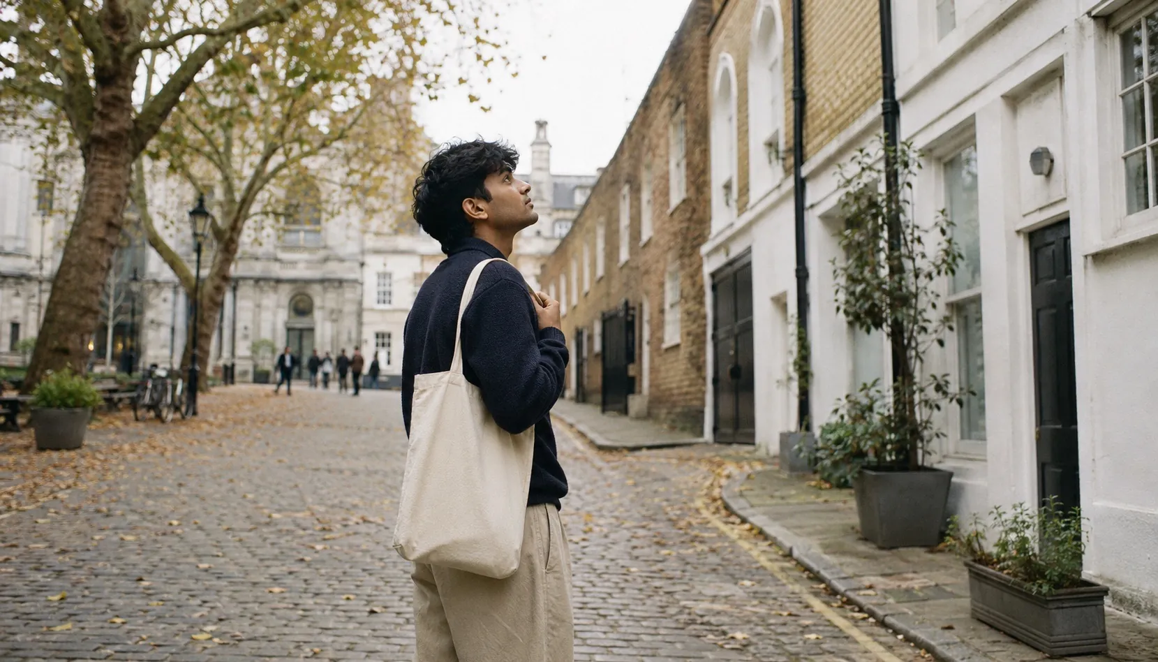 A student walking through a quiet cobbled London mews street in autumn, plane trees turning yellow, a soft grey sky